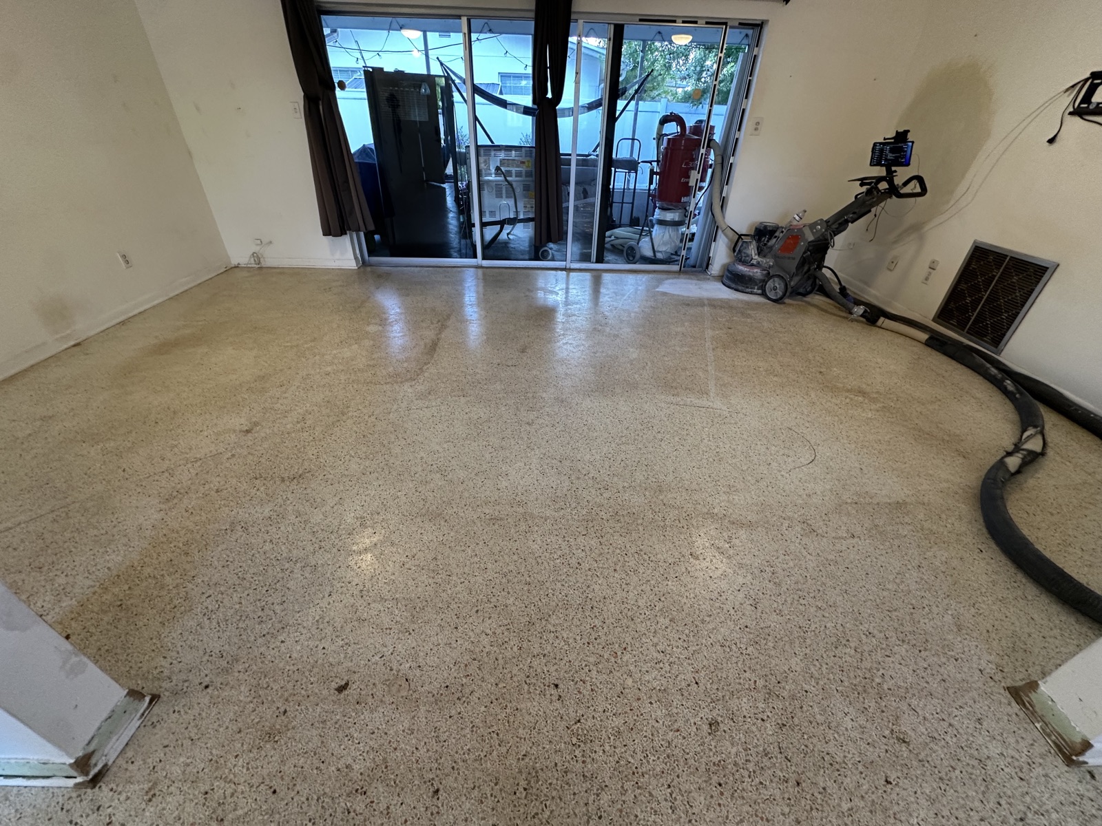 Living room terrazzo before restoration, stained after years under carpet, with the grinder set up by the sliding doors