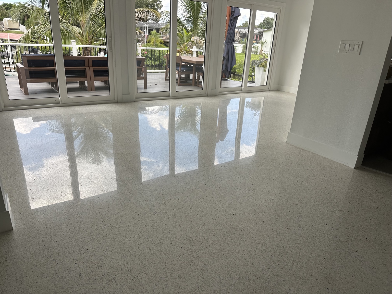 Polished terrazzo in front of the sliding glass doors to the back deck, with the palms reflected in the floor
