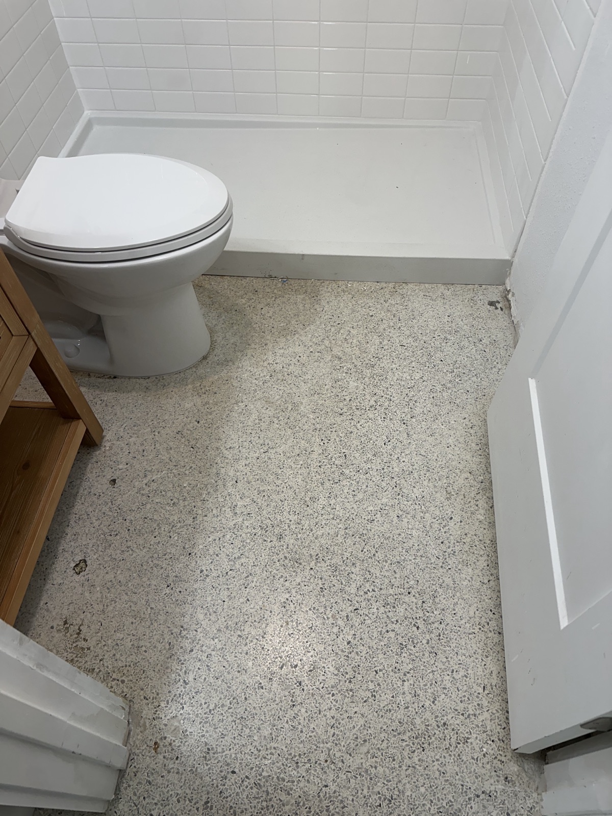 Bathroom terrazzo before the regrind, dull, with mismatched patches near the vanity and grime along the shower pan