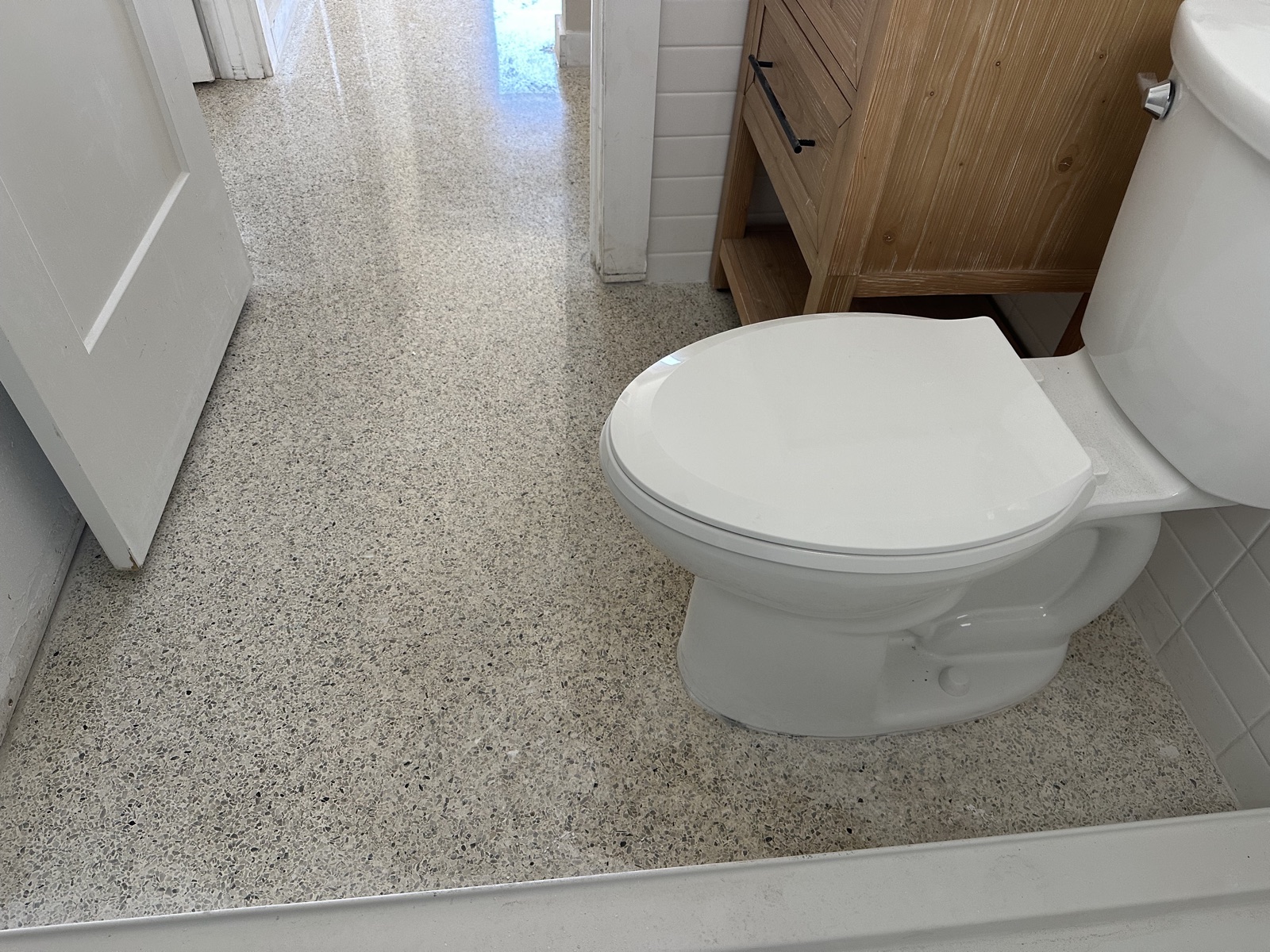 Bathroom floor by the toilet after polishing, looking out to the hallway