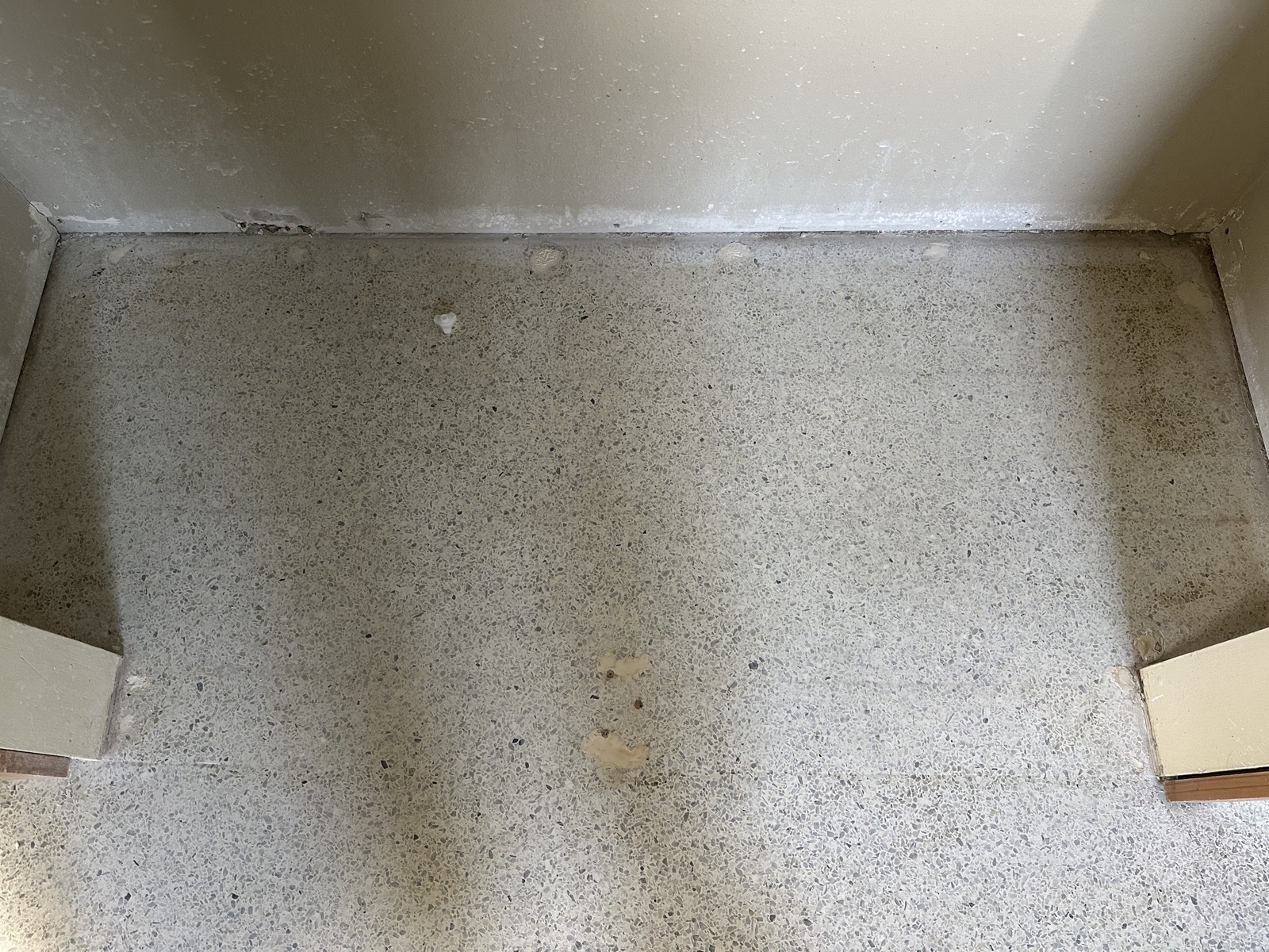 Closet floor before the regrind, with light patches that stand out from the terrazzo and a plastic anchor still in the floor