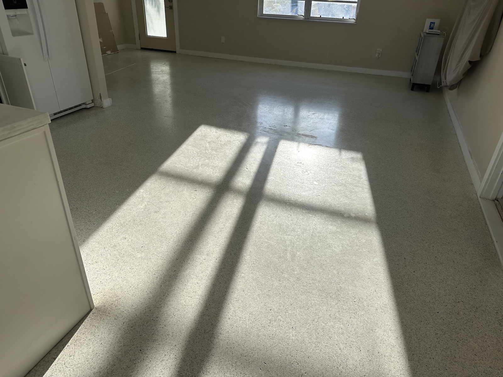 Living room terrazzo before the regrind, with swirl marks and scuffs in the finish showing where the sun hits it