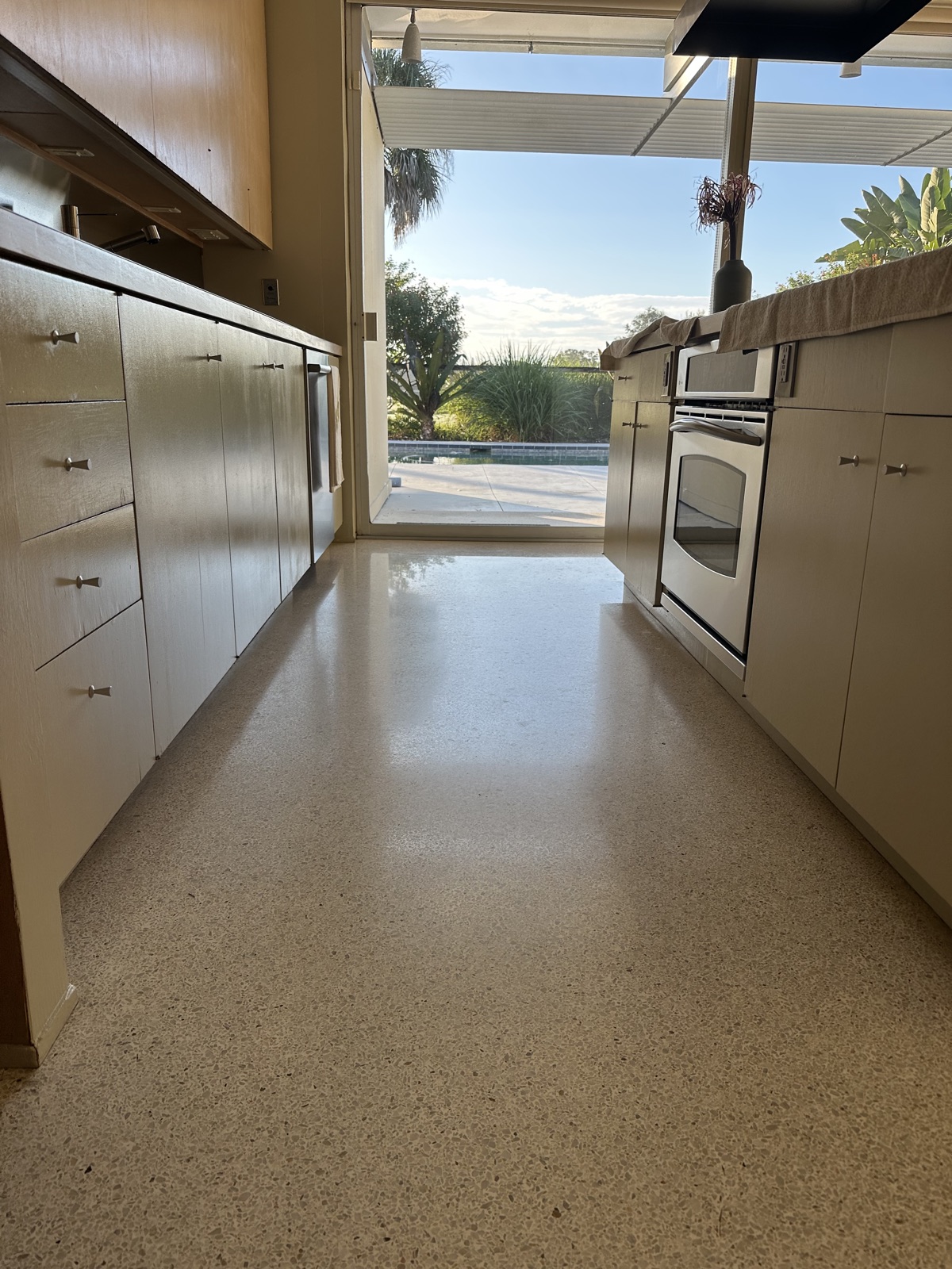 Galley kitchen terrazzo before repolishing, worn and dull between the cabinets.