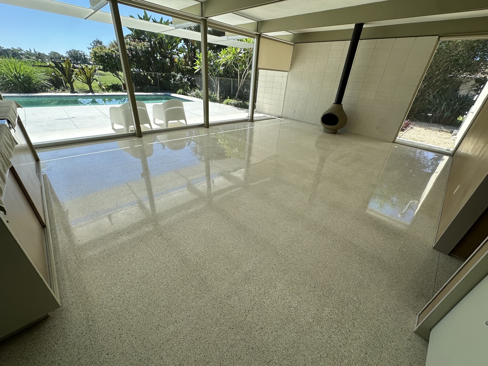 Living room terrazzo after repolishing, with the freestanding fireplace and glass wall behind it.
