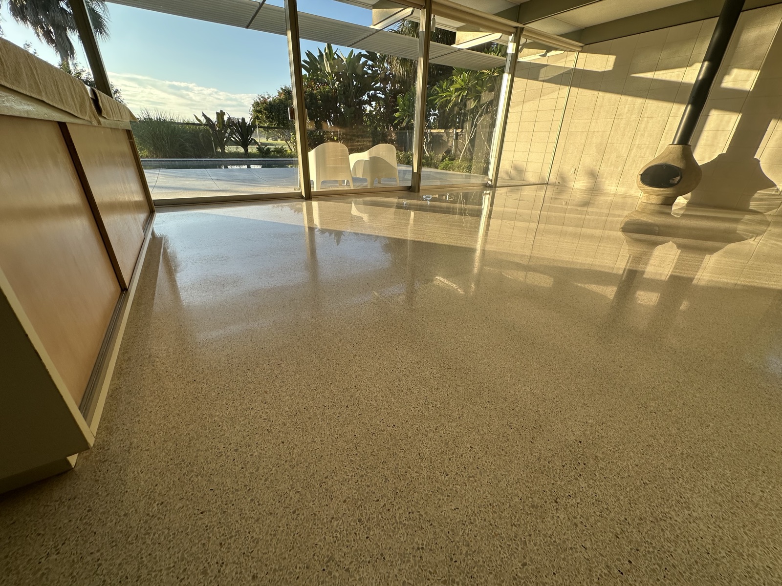 Living room terrazzo before repolishing, with the freestanding fireplace and glass wall in the background.