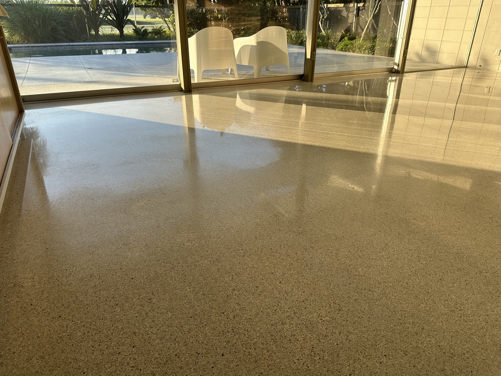 Living room terrazzo before repolishing, dull in the foreground, looking toward the glass wall and pool.